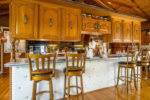 kitchen featuring vaulted ceiling, a kitchen breakfast bar, wood ceiling, kitchen peninsula, and light wood-type flooring