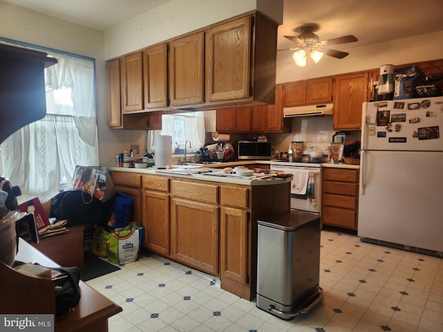 kitchen with under cabinet range hood, brown cabinets, a peninsula, white appliances, and a ceiling fan