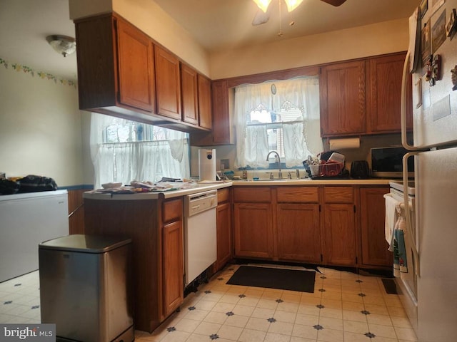 kitchen with white appliances, brown cabinetry, a wealth of natural light, and a sink