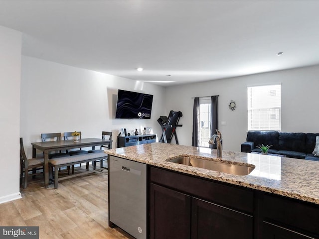 kitchen featuring sink, stainless steel dishwasher, light stone countertops, dark brown cabinets, and light wood-type flooring