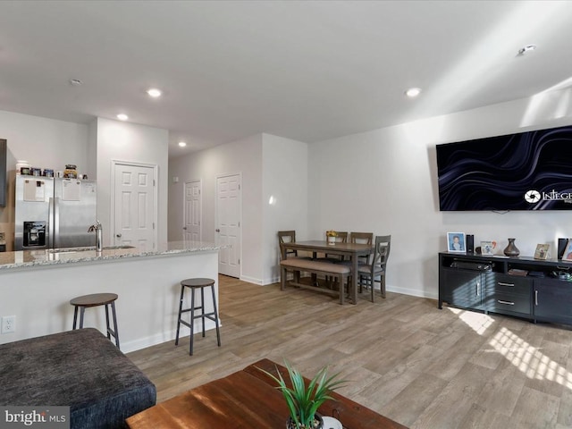 kitchen featuring a breakfast bar, sink, stainless steel fridge, light hardwood / wood-style floors, and light stone countertops