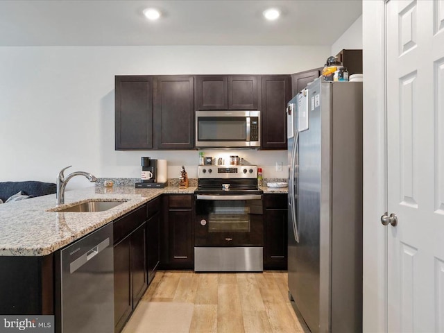 kitchen featuring sink, light stone counters, kitchen peninsula, stainless steel appliances, and light hardwood / wood-style flooring