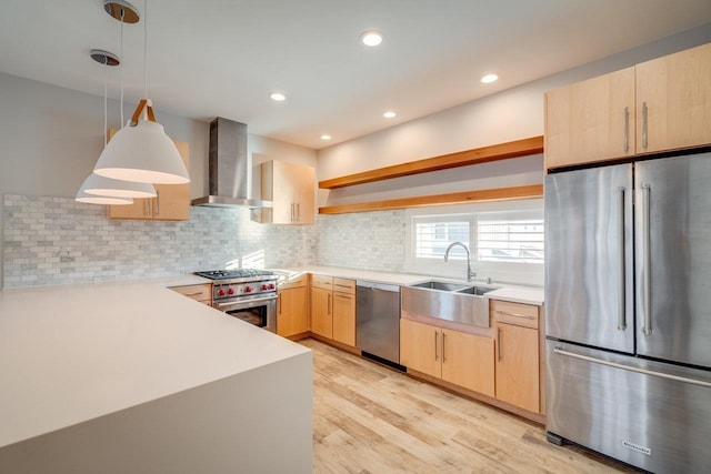 kitchen with sink, wall chimney range hood, hanging light fixtures, premium appliances, and light brown cabinetry