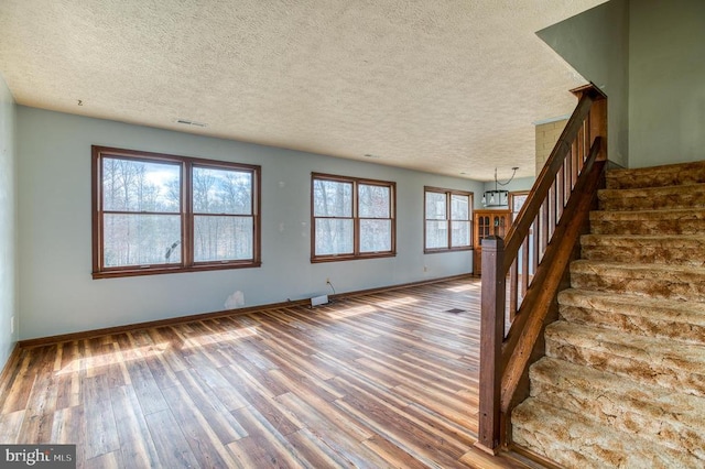 unfurnished living room featuring stairs, visible vents, baseboards, and wood finished floors