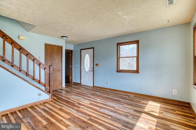 foyer entrance featuring a textured ceiling, wood finished floors, visible vents, baseboards, and stairs