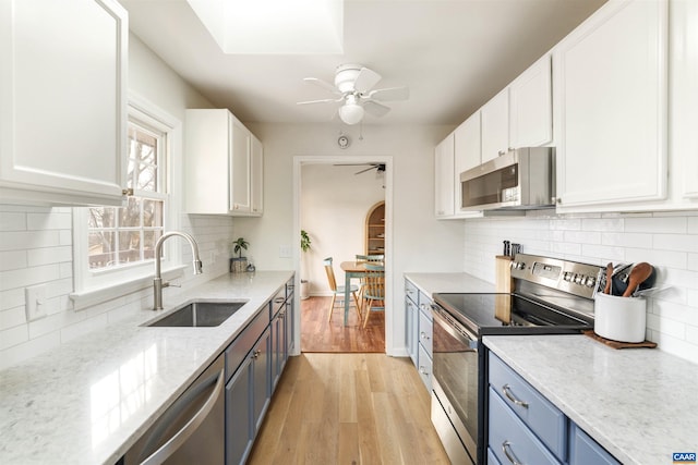 kitchen with ceiling fan, light wood-type flooring, appliances with stainless steel finishes, white cabinetry, and a sink