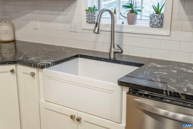 kitchen with white cabinetry, stainless steel dishwasher, dark stone counters, and tasteful backsplash