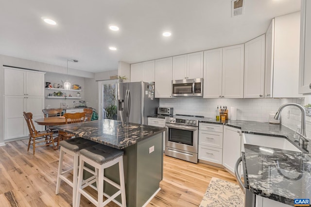 kitchen with sink, appliances with stainless steel finishes, white cabinetry, a center island, and a kitchen bar