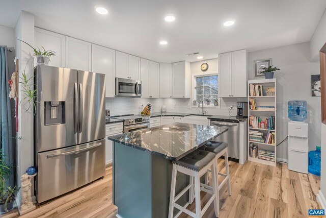 kitchen with dark stone countertops, a kitchen breakfast bar, stainless steel appliances, a center island, and white cabinets