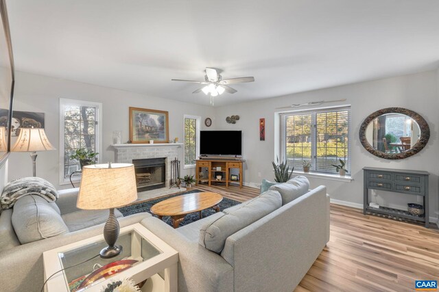 living room featuring ceiling fan, plenty of natural light, a fireplace, and light hardwood / wood-style floors