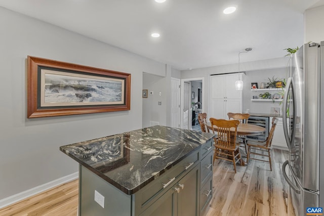 kitchen featuring decorative light fixtures, dark stone countertops, stainless steel fridge, a center island, and light hardwood / wood-style flooring