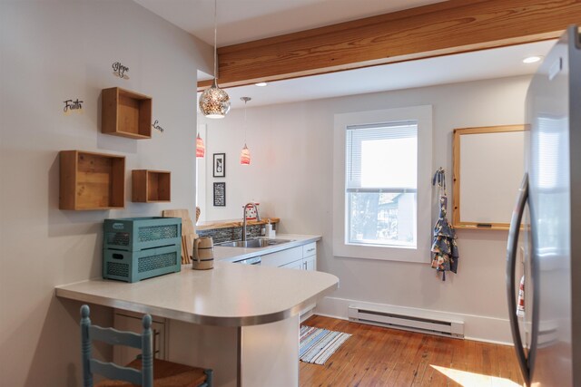 kitchen featuring sink, stainless steel fridge, kitchen peninsula, pendant lighting, and a baseboard heating unit