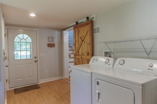 laundry area with independent washer and dryer, a barn door, and light wood-type flooring