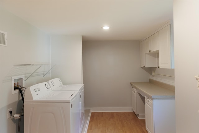 washroom featuring cabinets, washing machine and dryer, and light wood-type flooring