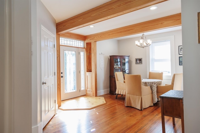 foyer with an inviting chandelier, plenty of natural light, beam ceiling, and light wood-type flooring