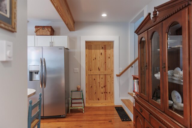 kitchen featuring beamed ceiling, light hardwood / wood-style floors, stainless steel fridge with ice dispenser, and white cabinets