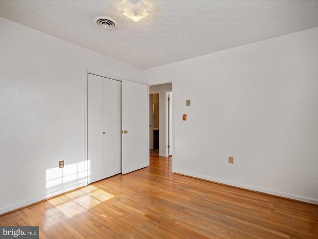 unfurnished bedroom featuring a textured ceiling, light wood-type flooring, and a closet