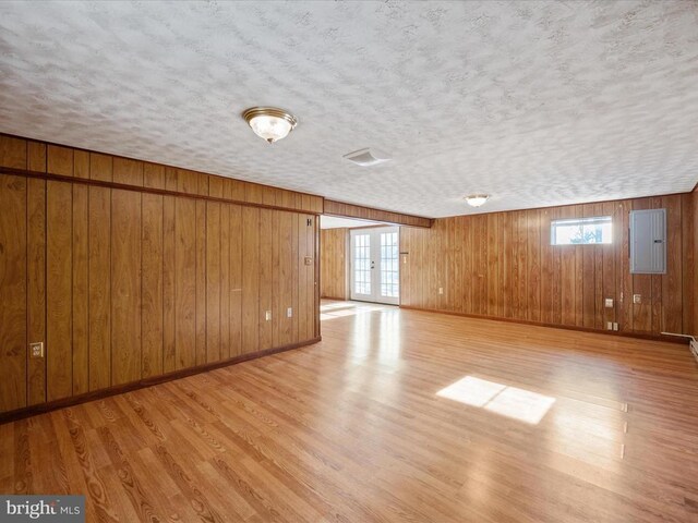 interior space with french doors, light hardwood / wood-style flooring, a textured ceiling, wooden walls, and electric panel