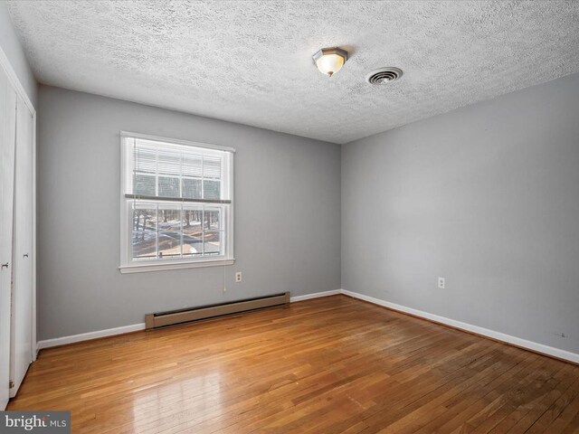 spare room featuring hardwood / wood-style flooring, a baseboard radiator, and a textured ceiling