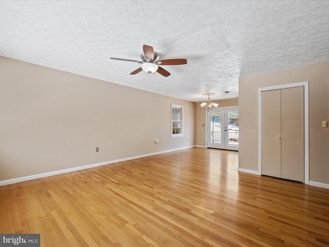 unfurnished living room featuring french doors, ceiling fan with notable chandelier, a textured ceiling, and light wood-type flooring