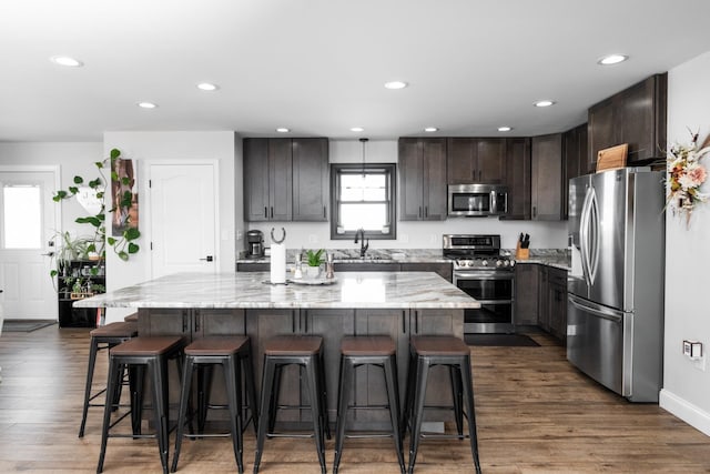 kitchen with sink, dark hardwood / wood-style floors, a kitchen island, stainless steel appliances, and light stone countertops