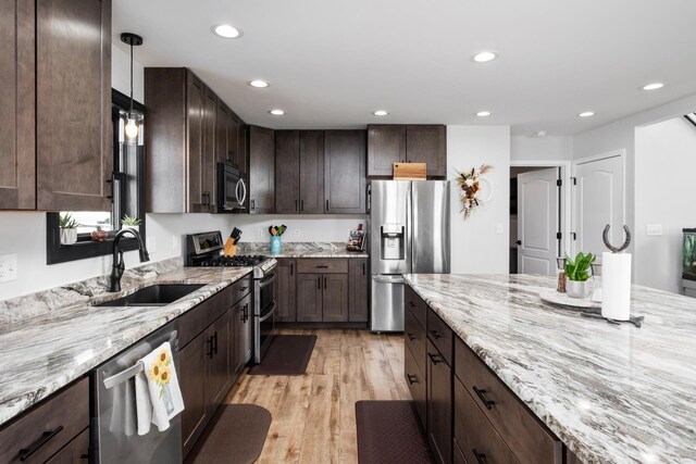 kitchen featuring appliances with stainless steel finishes, pendant lighting, sink, light stone countertops, and dark brown cabinets