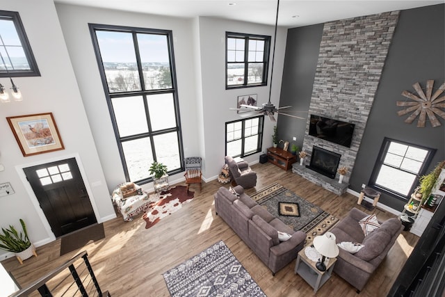 living room featuring a stone fireplace, light hardwood / wood-style flooring, ceiling fan, and a towering ceiling