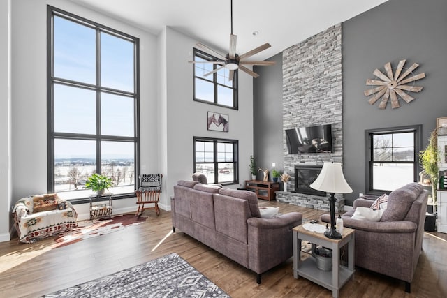 living room featuring hardwood / wood-style floors, a fireplace, ceiling fan, and a high ceiling