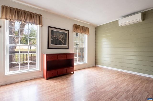 interior space with light wood-type flooring, a wall mounted air conditioner, and baseboards