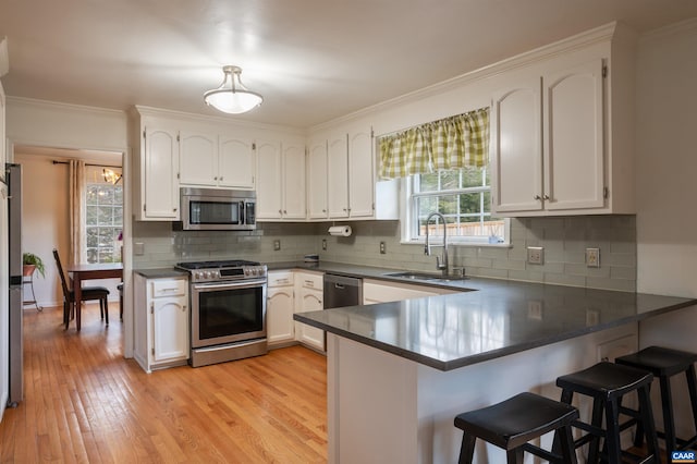 kitchen featuring appliances with stainless steel finishes, light wood-style floors, white cabinets, a sink, and a peninsula