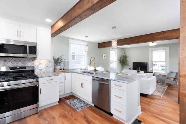 kitchen featuring appliances with stainless steel finishes, a peninsula, white cabinets, light wood finished floors, and light stone countertops