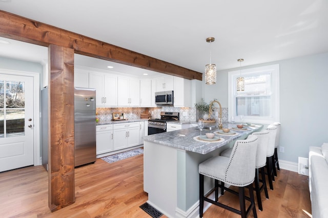 kitchen featuring backsplash, a breakfast bar area, a peninsula, stainless steel appliances, and white cabinetry