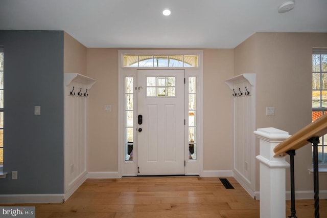 foyer entrance with visible vents, baseboards, light wood-style floors, and stairs