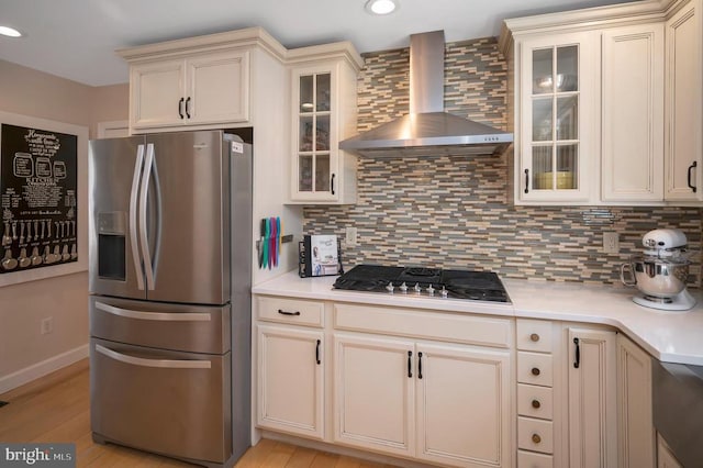 kitchen featuring light countertops, cream cabinetry, appliances with stainless steel finishes, wall chimney range hood, and backsplash