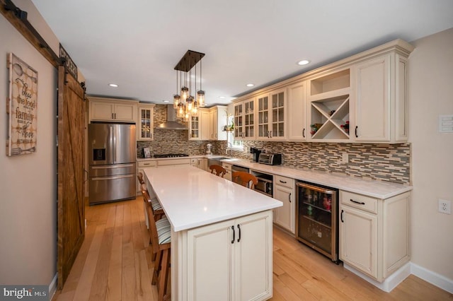 kitchen featuring beverage cooler, stainless steel refrigerator with ice dispenser, gas cooktop, a barn door, and wall chimney range hood