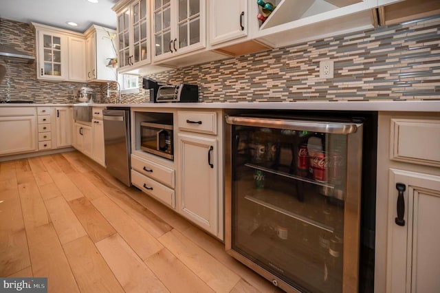 kitchen featuring light countertops, wine cooler, appliances with stainless steel finishes, light wood-type flooring, and backsplash