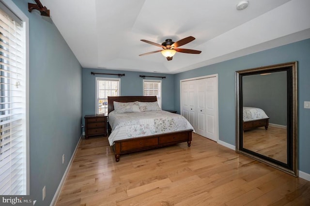 bedroom featuring ceiling fan, baseboards, light wood-style floors, and a tray ceiling