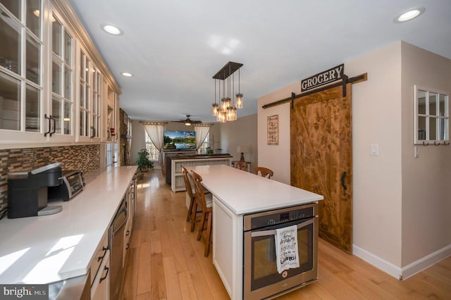 kitchen with light wood-type flooring, a barn door, light countertops, stainless steel oven, and ceiling fan