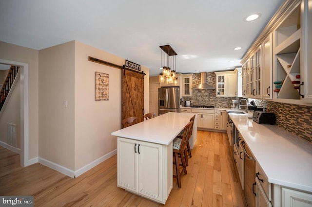 kitchen featuring tasteful backsplash, a barn door, wall chimney exhaust hood, stainless steel fridge, and gas cooktop