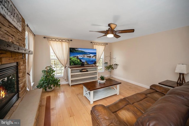 living room featuring light wood-type flooring, baseboards, and a stone fireplace