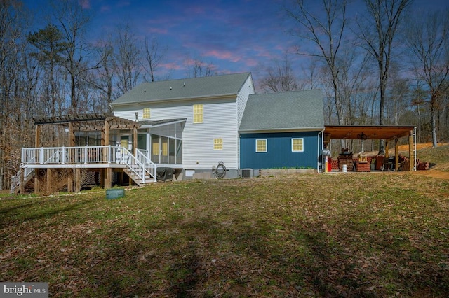 back of property at dusk featuring stairway, a pergola, central AC, and a yard