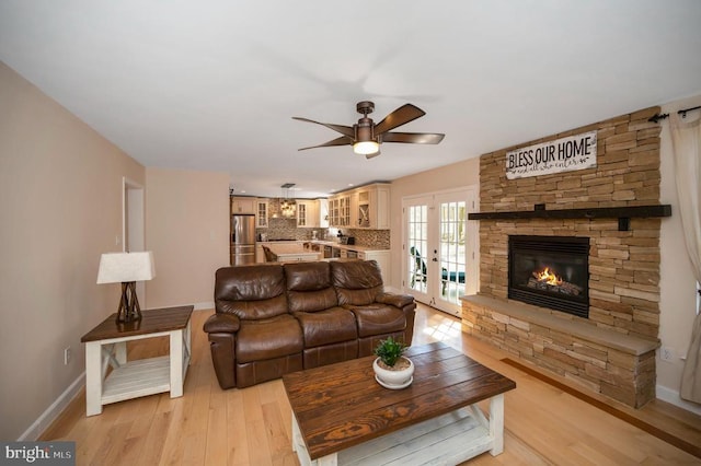 living room featuring french doors, baseboards, a fireplace, and light wood finished floors