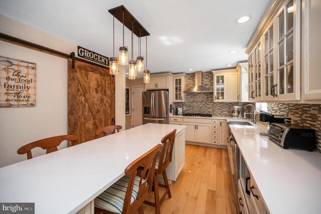 kitchen featuring a sink, appliances with stainless steel finishes, a kitchen bar, a barn door, and wall chimney exhaust hood