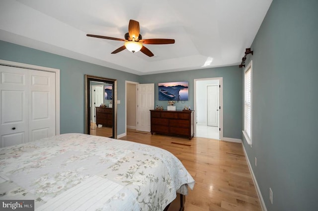 bedroom with a raised ceiling, a closet, light wood-style floors, baseboards, and ceiling fan