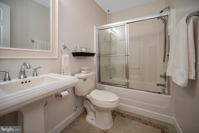 bathroom with baseboards, toilet, tile patterned floors, combined bath / shower with glass door, and a sink