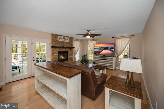 living room featuring light wood finished floors, a stone fireplace, a healthy amount of sunlight, and baseboards