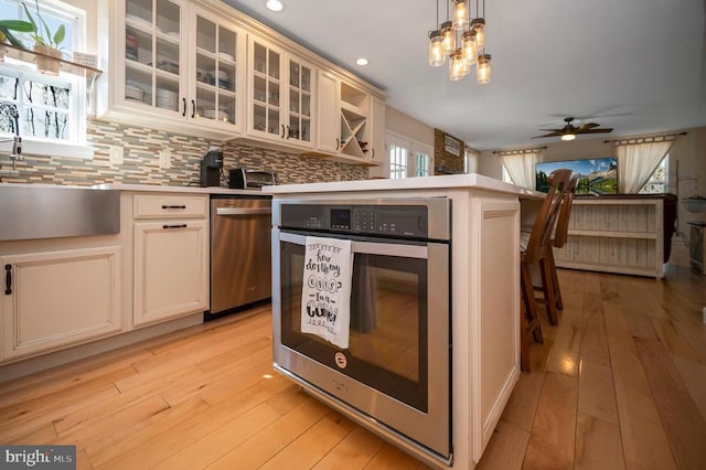 kitchen featuring light wood finished floors, cream cabinets, light countertops, decorative backsplash, and hanging light fixtures