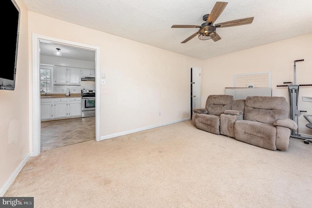 living room with light carpet, ceiling fan, a textured ceiling, and baseboards