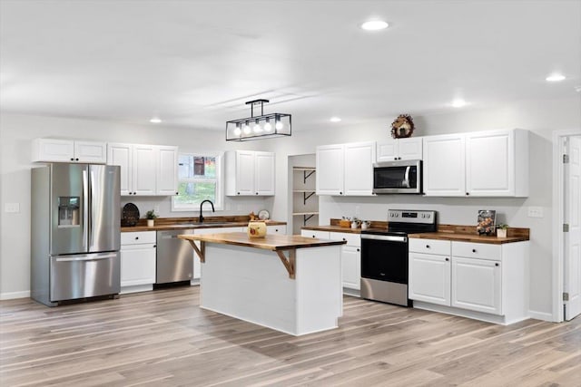 kitchen with appliances with stainless steel finishes, a sink, white cabinetry, and butcher block counters