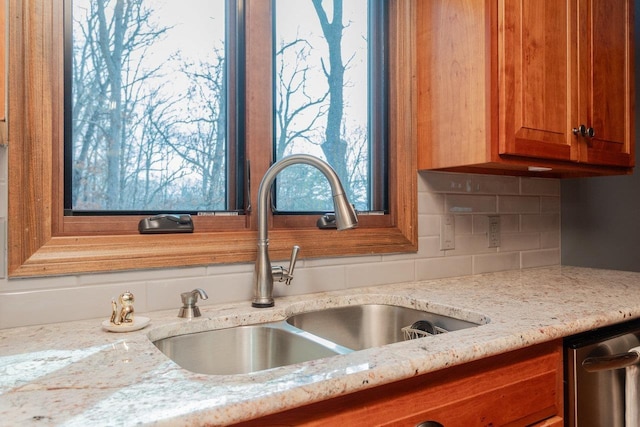 details featuring tasteful backsplash, light stone counters, brown cabinets, and a sink